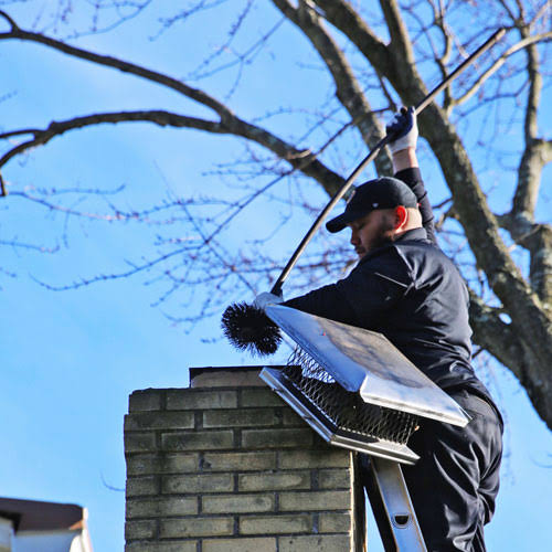 A person working beside a removed metal chimney cap with a cleaning brush