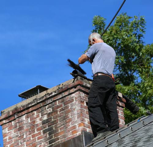 Brick chimney masonry and a person working at the top from a shingled roof